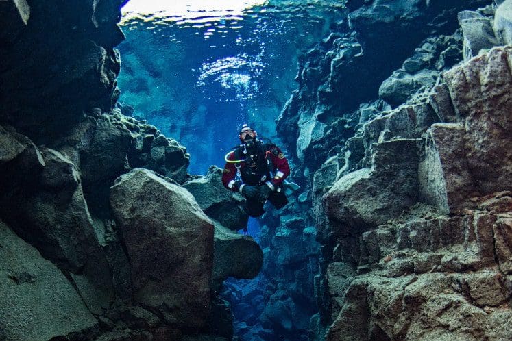 scuba diver between rocks exploring thingvellir lake silfra iceland